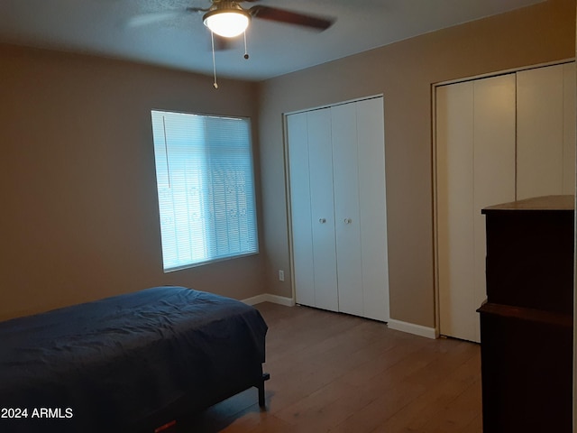 bedroom featuring two closets, light hardwood / wood-style flooring, and ceiling fan