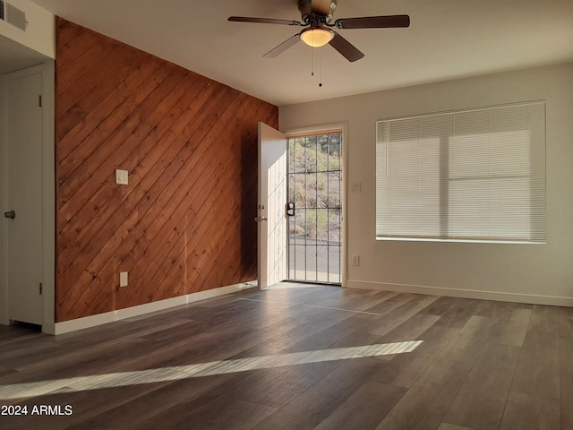 unfurnished room with dark wood-type flooring, ceiling fan, and wood walls