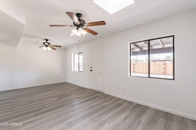 spare room with a skylight, ceiling fan, and light hardwood / wood-style floors