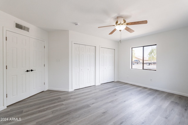 unfurnished bedroom with ceiling fan, light hardwood / wood-style floors, and multiple closets