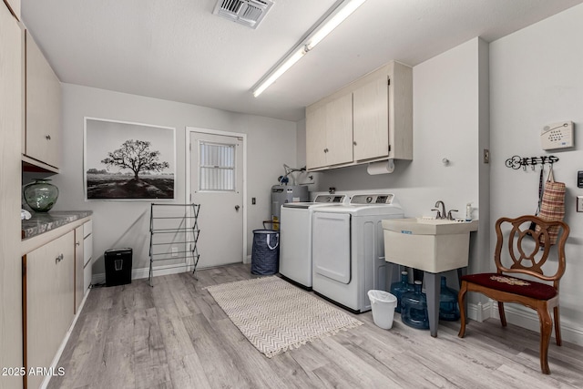 laundry area with light wood-style flooring, visible vents, water heater, cabinet space, and washer and dryer