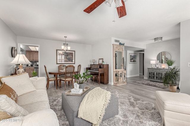 living area with baseboards, light wood-style floors, visible vents, and ceiling fan with notable chandelier