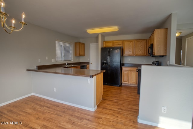 kitchen with sink, a notable chandelier, kitchen peninsula, light hardwood / wood-style floors, and black appliances