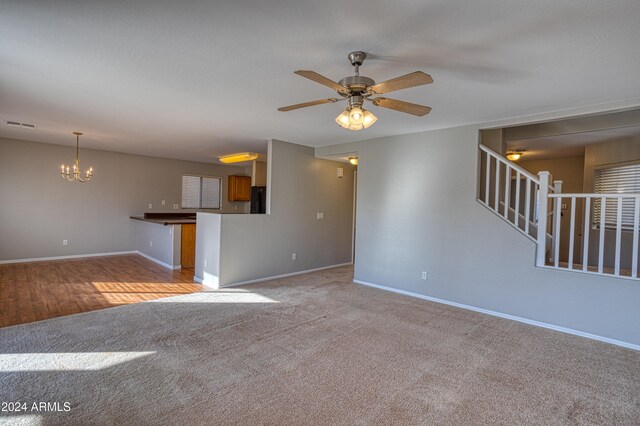 unfurnished living room with ceiling fan with notable chandelier and light carpet