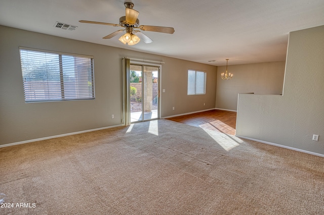 carpeted spare room with ceiling fan with notable chandelier