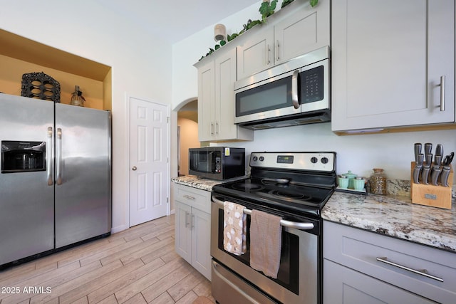 11207 W Turney Ave, Phoenix, AZ 85037 - kitchen featuring appliances with stainless steel finishes, arched walkways, light wood-type flooring, light stone countertops, and gray cabinets