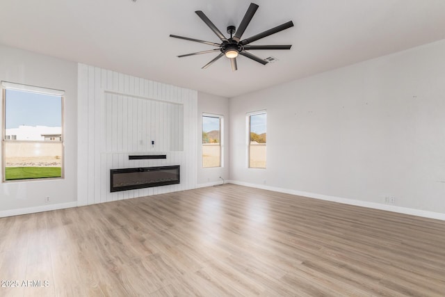 unfurnished living room with a large fireplace, ceiling fan, baseboards, and light wood-style floors