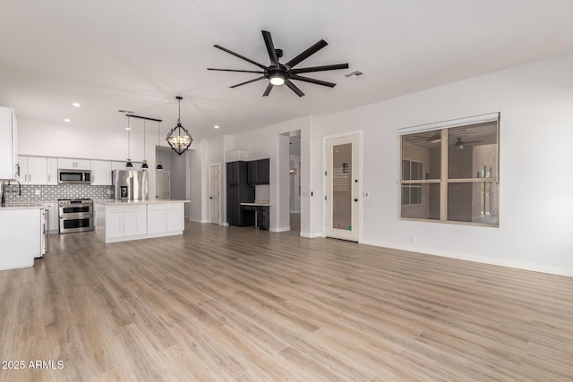 unfurnished living room with visible vents, a sink, light wood-type flooring, baseboards, and ceiling fan with notable chandelier