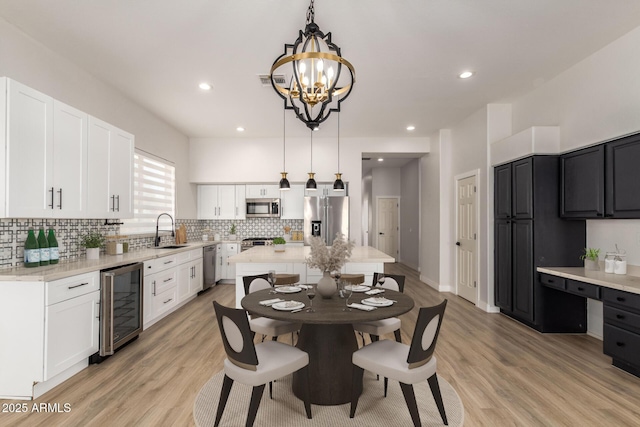 kitchen featuring beverage cooler, stainless steel appliances, white cabinetry, backsplash, and decorative light fixtures