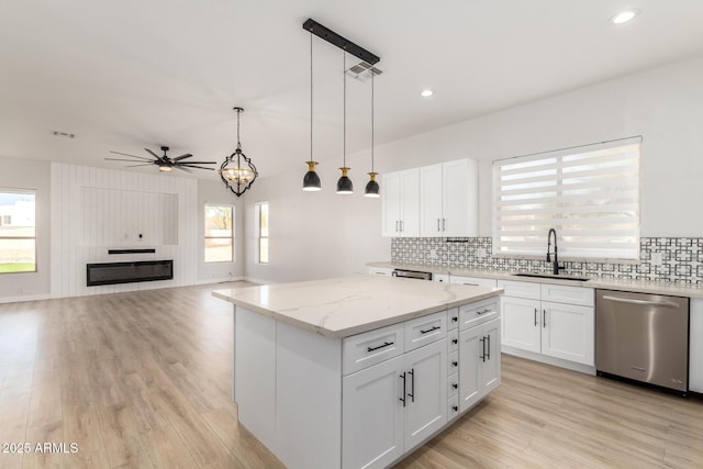 kitchen featuring a kitchen island, a sink, white cabinetry, open floor plan, and stainless steel dishwasher