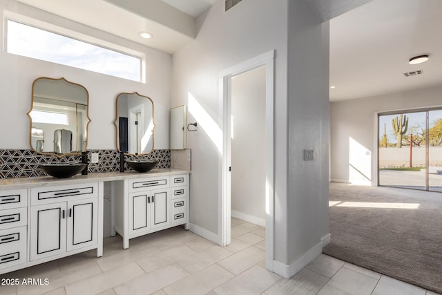 bathroom with double vanity, baseboards, visible vents, backsplash, and a sink