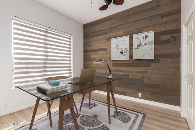office area with wood walls, ceiling fan, baseboards, and wood finished floors