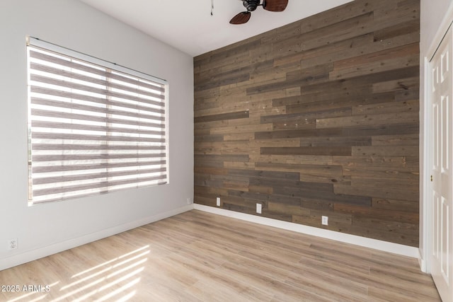 empty room featuring baseboards, wood walls, a ceiling fan, and light wood-style floors