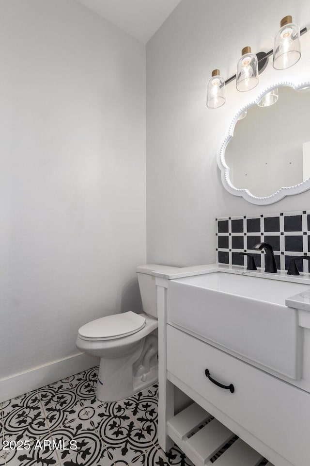 half bathroom featuring tile patterned flooring, baseboards, vanity, and toilet