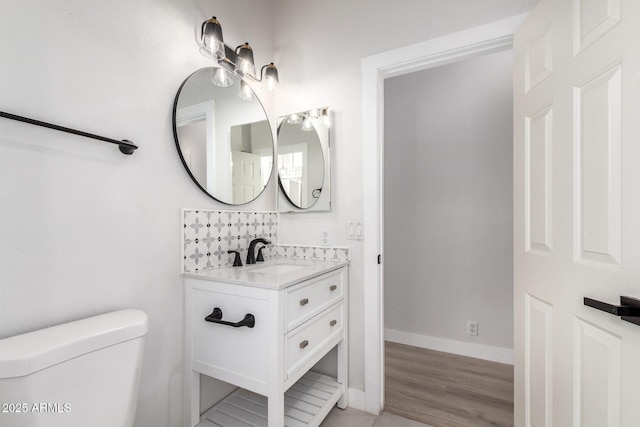 half bath featuring toilet, baseboards, wood finished floors, and vanity