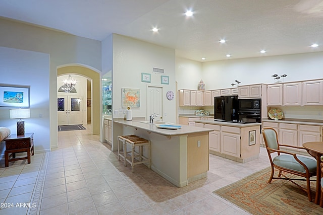 kitchen with light tile patterned flooring, a high ceiling, black appliances, and an island with sink