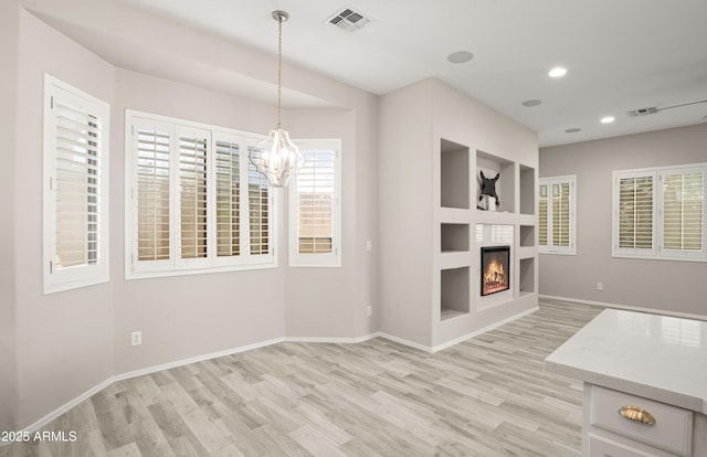 unfurnished living room with light wood-style floors, a glass covered fireplace, baseboards, recessed lighting, and a chandelier