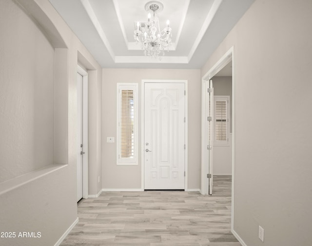 foyer featuring a chandelier, light wood-style floors, a tray ceiling, and baseboards