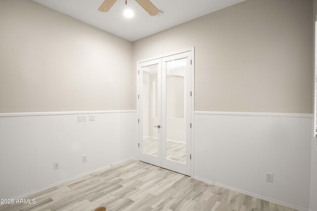unfurnished bedroom with wood finished floors, a wainscoted wall, french doors, and ceiling fan