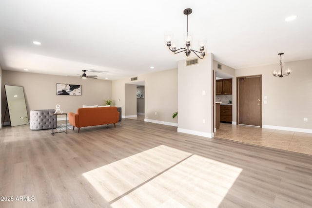 unfurnished living room with ceiling fan with notable chandelier and light wood-type flooring