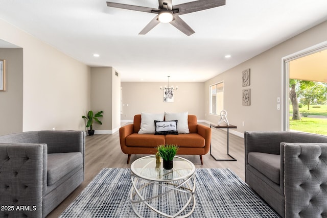 living room featuring ceiling fan with notable chandelier and light hardwood / wood-style floors