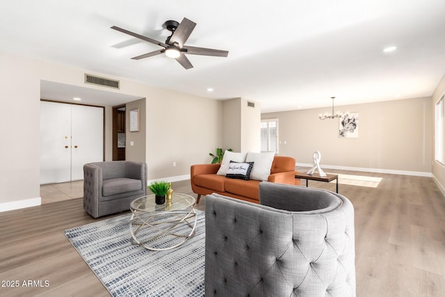 living room featuring ceiling fan with notable chandelier and light wood-type flooring