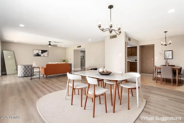 dining space with ceiling fan with notable chandelier and light hardwood / wood-style floors