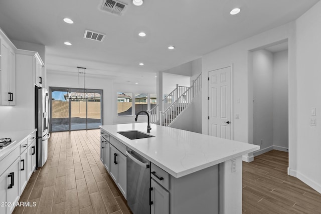 kitchen with sink, hanging light fixtures, stainless steel appliances, dark hardwood / wood-style flooring, and a kitchen island with sink