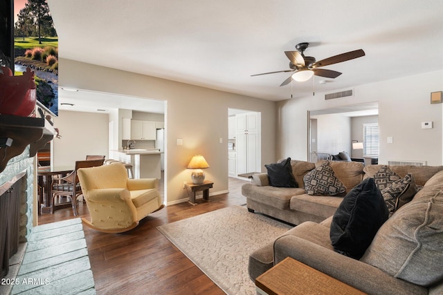 living room featuring sink, ceiling fan, a stone fireplace, and dark hardwood / wood-style flooring