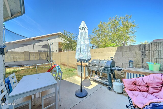 view of patio / terrace featuring a fenced backyard, a trampoline, a grill, and outdoor dining space