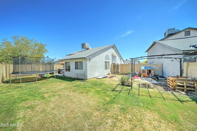 back of house featuring a pergola, a fenced backyard, central AC unit, a lawn, and a trampoline