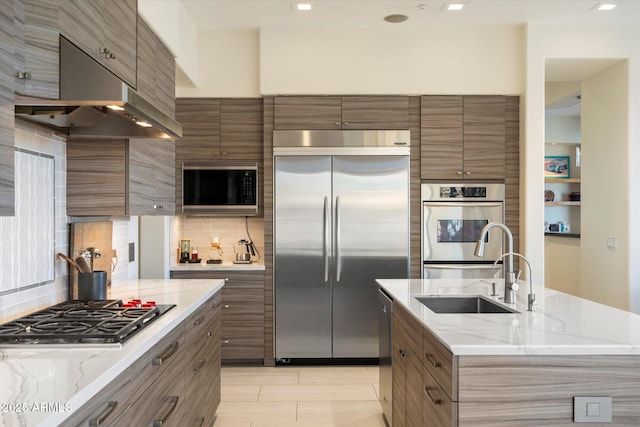 kitchen featuring under cabinet range hood, brown cabinetry, built in appliances, and a sink