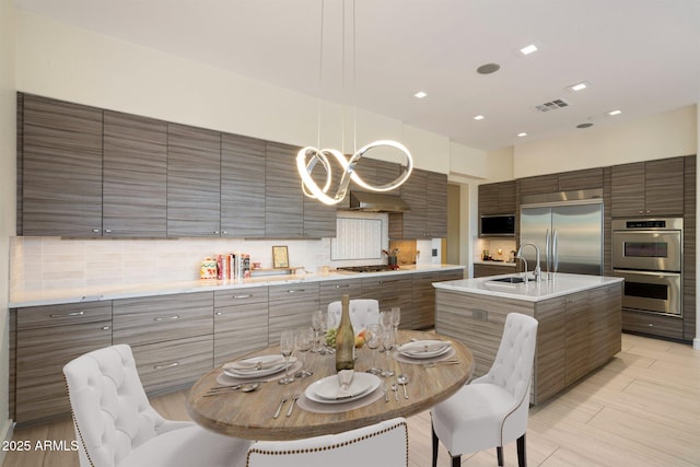 kitchen featuring a sink, built in appliances, modern cabinets, and a center island with sink