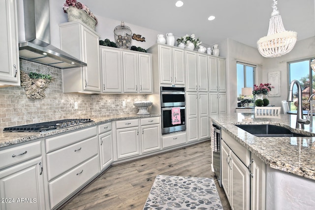 kitchen featuring light hardwood / wood-style flooring, appliances with stainless steel finishes, sink, white cabinetry, and wall chimney range hood