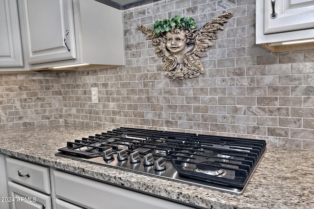 kitchen with stainless steel gas stovetop, light stone counters, decorative backsplash, and white cabinets