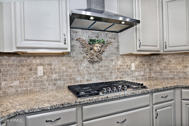 kitchen featuring stainless steel gas stovetop, light stone counters, decorative backsplash, and wall chimney exhaust hood