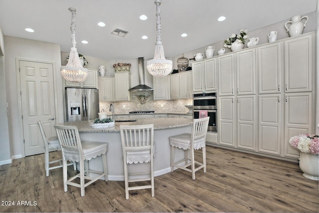 kitchen featuring wood-type flooring, stainless steel appliances, an inviting chandelier, and wall chimney range hood