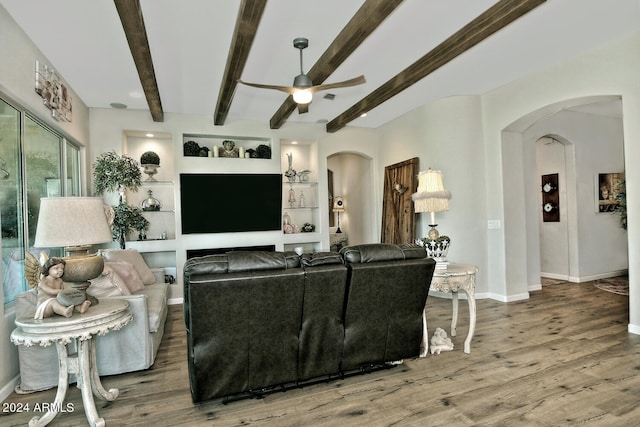 living room with built in features, ceiling fan, beamed ceiling, and wood-type flooring