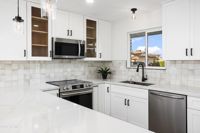 kitchen with stainless steel appliances, a sink, white cabinets, hanging light fixtures, and glass insert cabinets