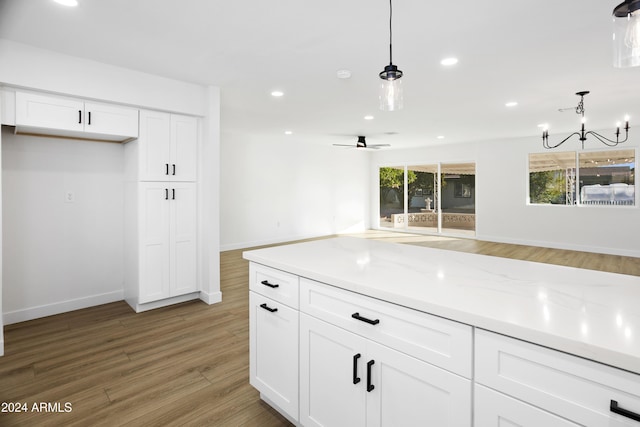 kitchen featuring open floor plan, white cabinetry, hanging light fixtures, and light stone countertops