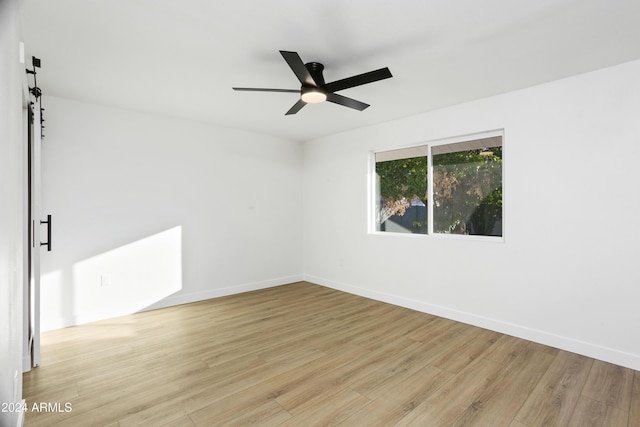 empty room featuring light wood-type flooring, ceiling fan, baseboards, and a barn door