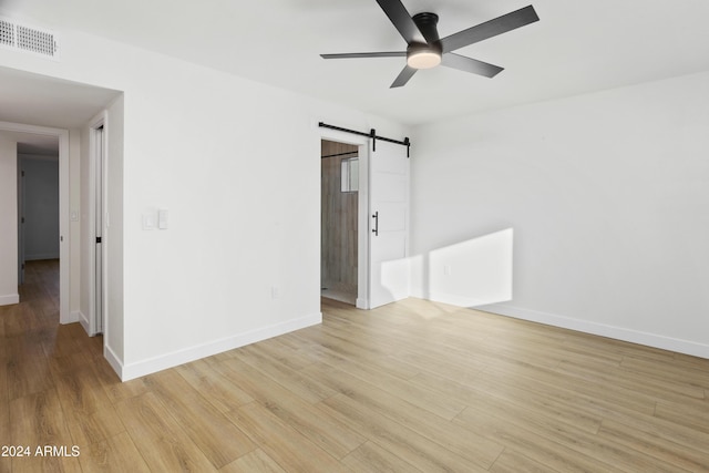 empty room with visible vents, ceiling fan, light wood finished floors, and a barn door