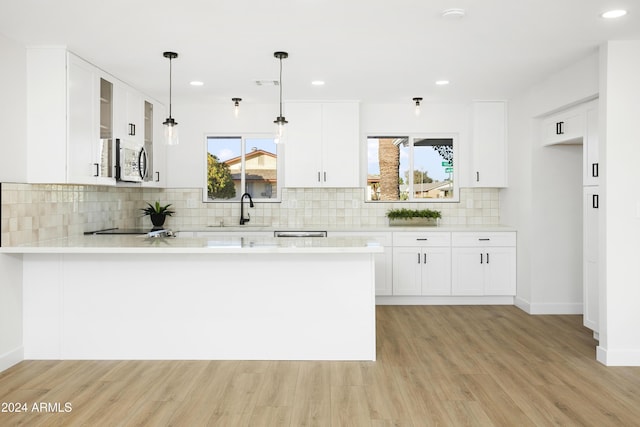 kitchen featuring light countertops, stainless steel microwave, white cabinets, a sink, and a peninsula