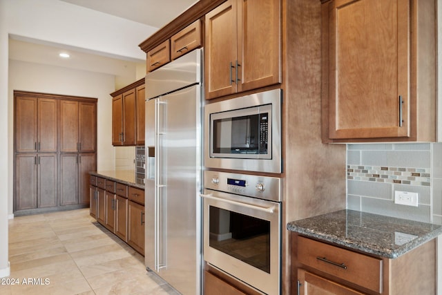 kitchen featuring dark stone counters, built in appliances, and backsplash