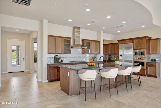 kitchen with built in appliances, a breakfast bar, wall chimney exhaust hood, backsplash, and a large island