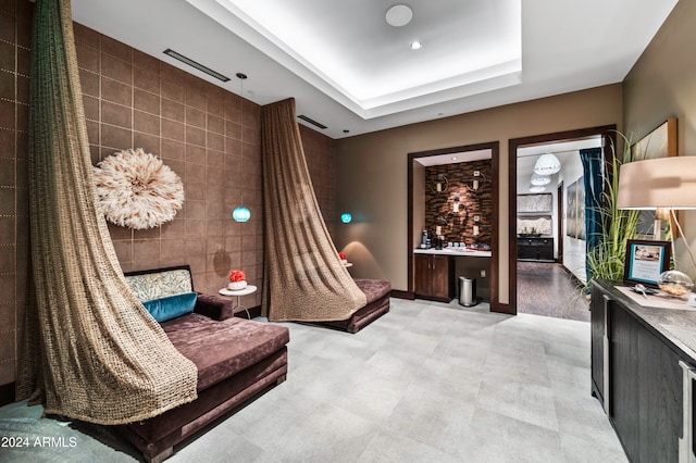 sitting room featuring a raised ceiling and tile walls