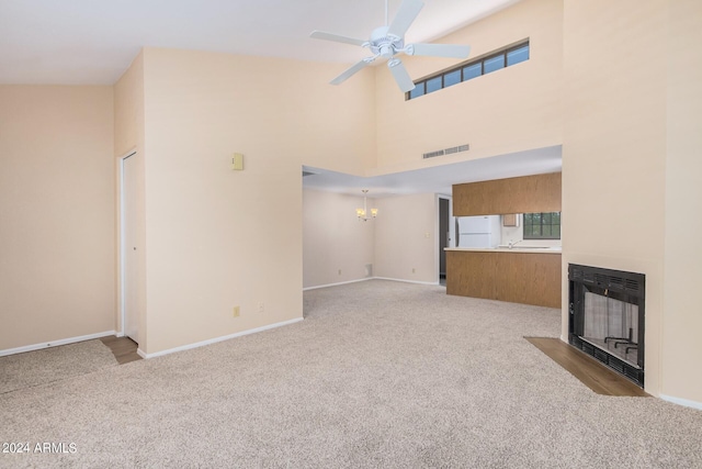 unfurnished living room featuring ceiling fan with notable chandelier, a high ceiling, and light carpet