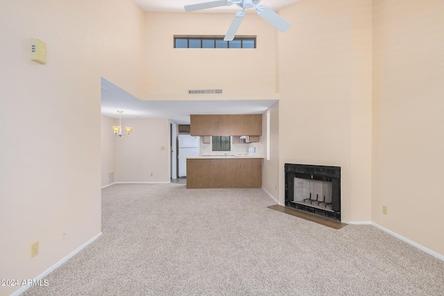 unfurnished living room with light carpet, ceiling fan with notable chandelier, and a towering ceiling