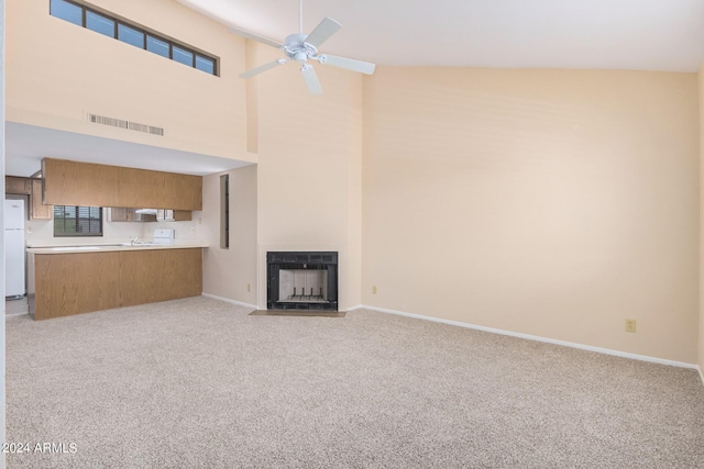 unfurnished living room featuring ceiling fan, light carpet, and a towering ceiling