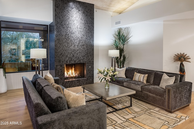 living room featuring high vaulted ceiling, a fireplace, light hardwood / wood-style floors, and wood ceiling